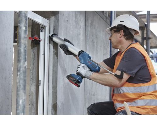 Ein Bauarbeiter verwendet eine Akku-Kartuschenpistole zum Abdichten eines Fensters.