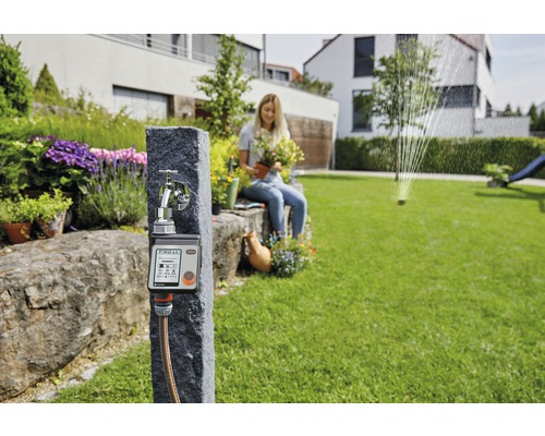Gardena Wasserhahn mit Bewässerungssteuerung und Frau mit Pflanze im Garten