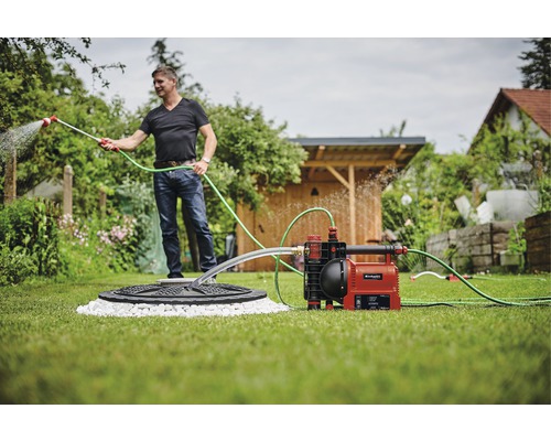 Garten mit Hauswasserwerk, Mann mit Gartenschlauch bewässert den Garten