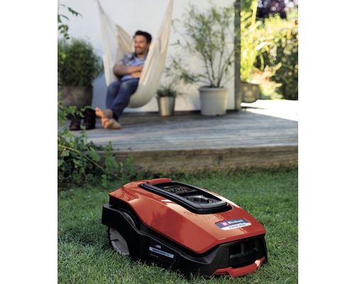 Rasenmäherroboter im Garten mit entspanntem Mann in Hängematte