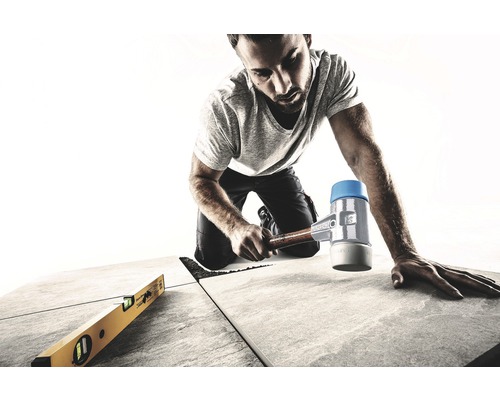 Handwerker verlegt Fliesen mit Gummihammer und Wasserwaage