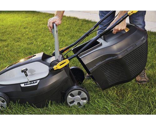 Eine Person befestigt den Fangkorb an einem Rasenmäher auf einer Rasenfläche.