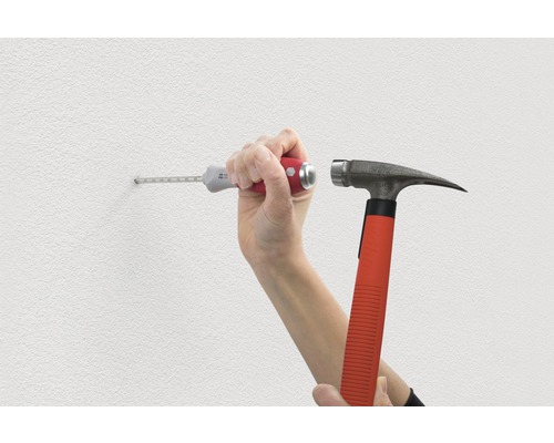 Eine Person, die mit Hammer und Dübel ein Loch in eine Wand schlägt.