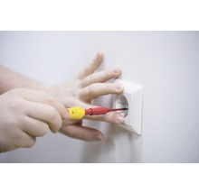 Eine Hand führt mit einem Schraubendreher Elektroarbeiten an einer Steckdose durch.
