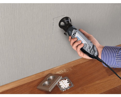 Eine Person verwendet ein Dremel Werkzeug, um eine Aussparung in eine Wand zu schneiden, wobei sich eine Steckdose in der Nähe befindet.