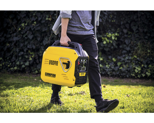 Eine Person trägt einen gelben Champion Stromerzeuger mit 2200 Watt Leistung im Garten.