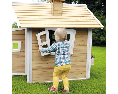 Kind öffnet Fenster an einem Holzspielhaus im Garten.