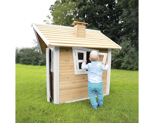 Kind spielt mit einem Holzspielhaus im Garten.