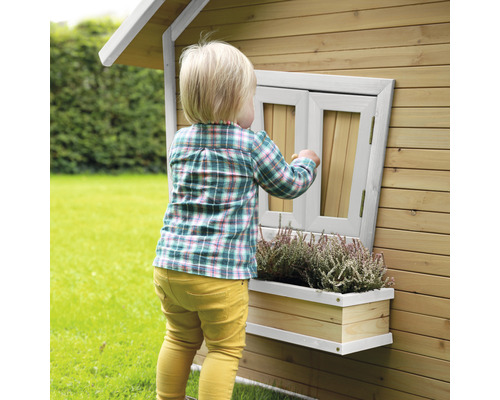 Ein Kind spielt an einem Holzspielhaus mit Fenster und Blumenkasten im Garten.
