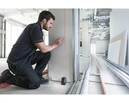 Handwerker markiert mit einem Bleistift eine Linie an einer Gipskartonwand, die mit einem Linienlaser erzeugt wurde.