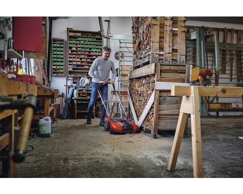 Ein Mann benutzt einen Rasenlüfter in einer Werkstatt voller Holz und Werkzeuge.