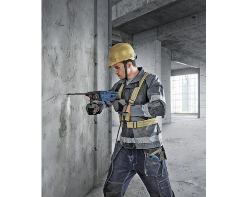 Ein Bauarbeiter bohrt mit einem Bohrhammer in eine Betonwand. Der Mann trägt einen Schutzhelm und Sicherheitskleidung.