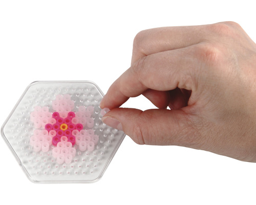Person fügt eine Bügelperle auf eine sechseckige Stiftplatte mit Blumenmuster.