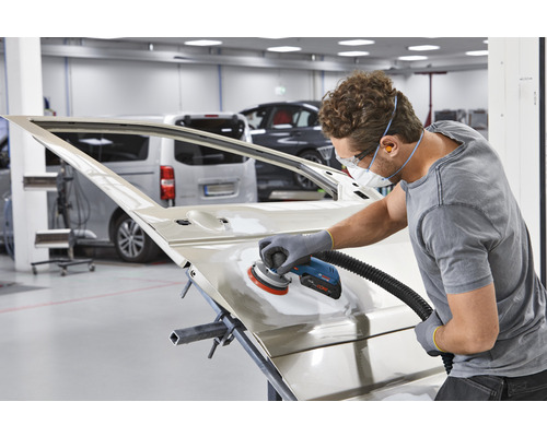 Ein Mann schleift eine Autotür mit einem Schleifgerät in einer Werkstatt.