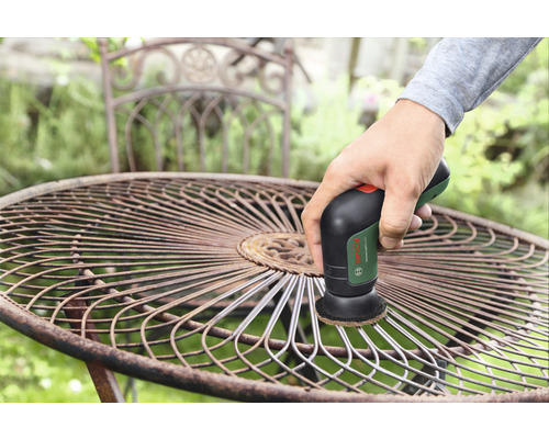 Eine Person reinigt einen Gartentisch aus Metall mit einem Schleifgerät von Bosch