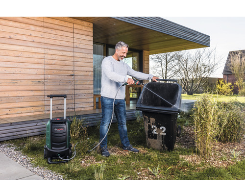 Mann reinigt Mülltonne mit Hochdruckreiniger im Garten.