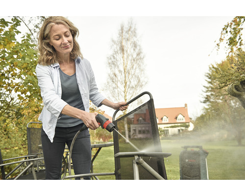 Frau reinigt Gartenmöbel mit einem Hochdruckreiniger im Freien