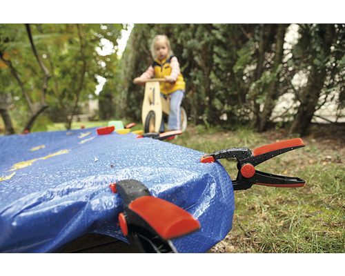 Abdeckplane mit Klammern im Garten, im Hintergrund Kind auf Laufrad