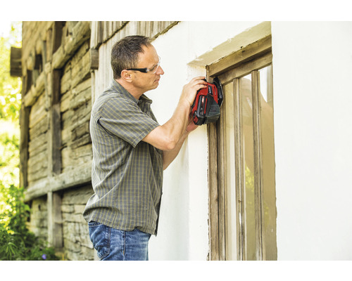 Ein Mann mit Schutzbrille renoviert ein Holzfenster mit einem Multifunktionswerkzeug.