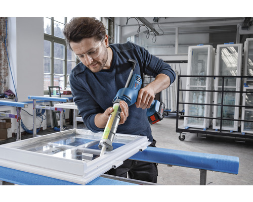 Ein Mann verwendet eine Akku-Kartuschenpistole, um Dichtungsmasse auf einen Fensterrahmen aufzutragen.