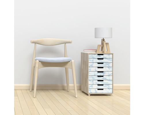 Szene mit einem Holzstuhl, einem Schubladenschrank mit Marmoroptik, einer Lampe und einem Buch