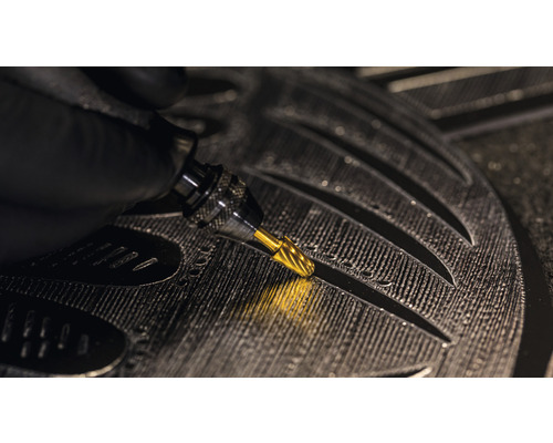 Nahaufnahme einer Hand mit einem Gravierstichel, der in ein Werkstück Details eingraviert.