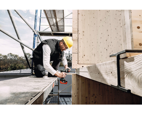 Handwerker auf einem Gerüst verschraubt Holzbalken mit einem Akku-Schrauber.