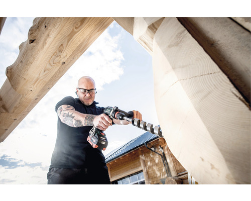 Ein Mann bohrt mit einem Akkubohrer ein Loch in einen Holzbalken.