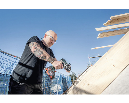 Handwerker arbeitet mit einem Akkuschrauber an einem Holzdach