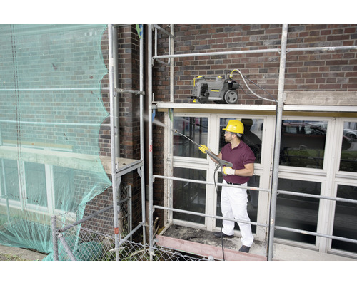 Mann auf Gerüst reinigt Fassade mit Hochdruckreiniger