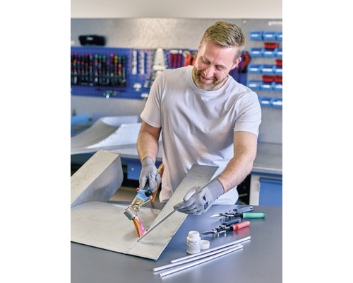 Mann lötet Metallblech mit Lötzubehör in Werkstatt