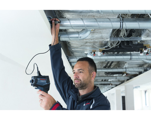 Ein Mann inspiziert mit einer Inspektionskamera Rohrleitungen unter einer Decke.