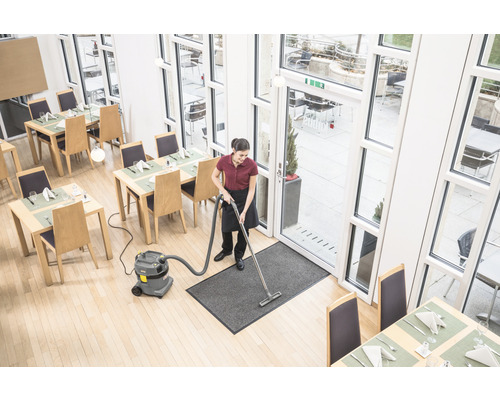 Eine Reinigungskraft saugt mit einem Mehrzwecksauger einen Eingangsteppich in einem Restaurant.