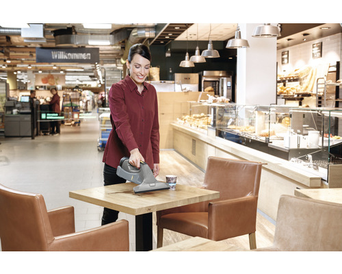 Eine Frau reinigt einen Tisch mit einem Akku-Fenstersauger in einem Café.