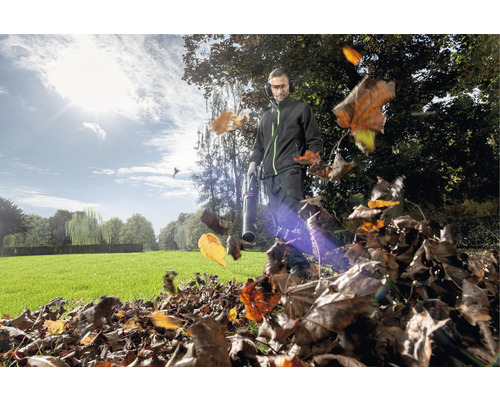 Ein Mann benutzt einen Laubbläser im Garten, um Herbstlaub zusammenzutragen.