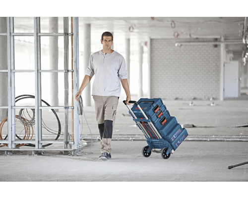 Handwerker zieht einen Werkzeugkofferwagen von Bosch durch eine Baustelle.