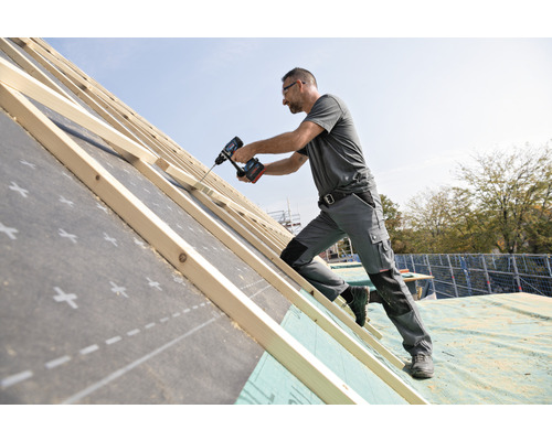 Handwerker arbeitet mit einem Akkuschrauber auf einem Dachstuhl.