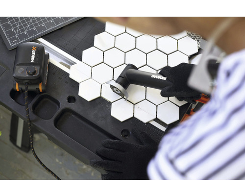 Eine Person schneidet sechseckige Fliesen mit einem Fliesenschneider auf einer Werkbank.