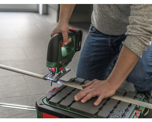 Eine Person schneidet ein Rohr mit einer Akku-Stichsäge auf einem Sägetisch.