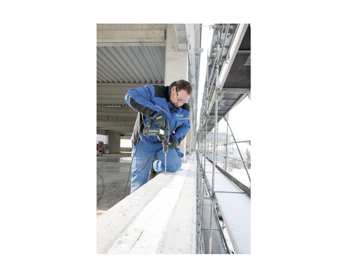 Ein Mann bohrt mit einer Metabo Bohrmaschine in einen Betonbalken auf einem Gerüst.