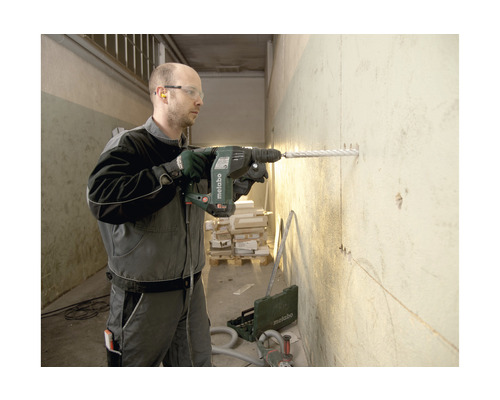 Ein Mann bohrt mit einem Metabo Bohrhammer ein Loch in eine Wand.