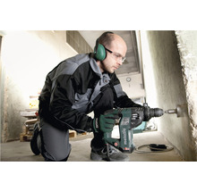 Ein Mann bohrt mit einer Metabo Bohrmaschine ein Loch in eine Betonwand. Er trägt dabei Gehörschutz und Schutzbrille.