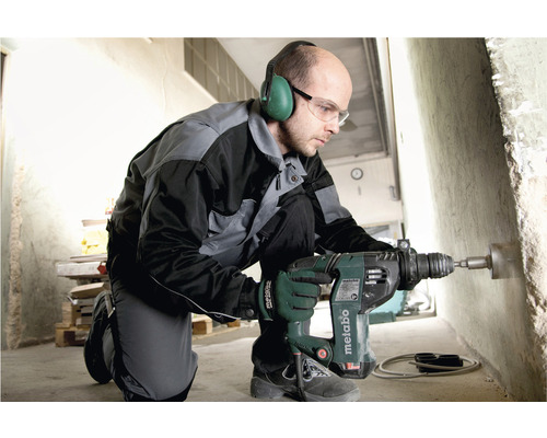 Ein Mann bohrt mit einer Metabo Bohrmaschine ein Loch in eine Betonwand. Er trägt dabei Gehörschutz und Schutzbrille.
