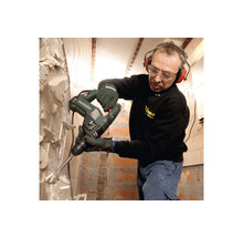 Mann mit Schutzbrille und Gehörschutz entfernt Fliesen mit einem Metabo Bohrhammer von der Wand.