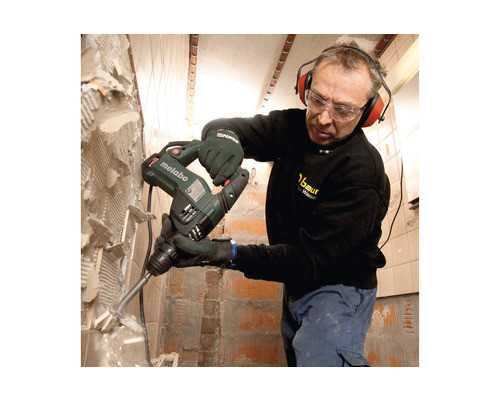 Mann mit Schutzbrille und Gehörschutz entfernt Fliesen mit einem Metabo Bohrhammer von der Wand.