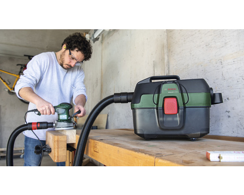 Handwerker beim Schleifen mit Schleifgerät und Staubsauger von Bosch auf einer Werkbank.