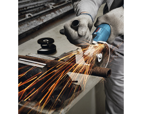 Eine Person schneidet mit einem Winkelschleifer ein Metallrohr. Funken fliegen.