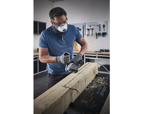 Ein Handwerker mit Schutzbrille und Atemschutzmaske sägt mit einer Mauernutfräse in ein Holzstück.