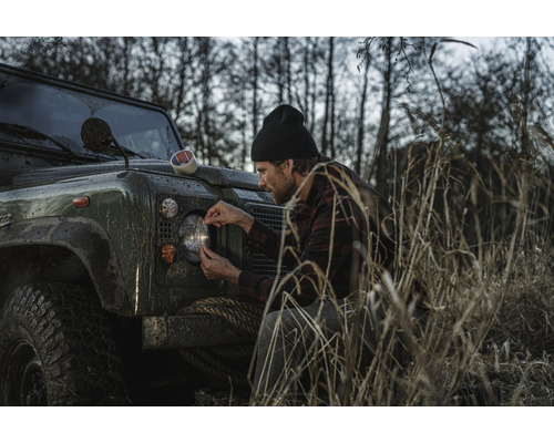 Mann befestigt Klebeband an Scheinwerfer von Geländewagen