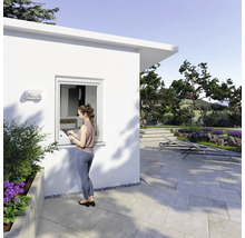 Frau steht vor einem Gartenhaus mit Kunststofffenster und genießt den Blick in den Garten.
